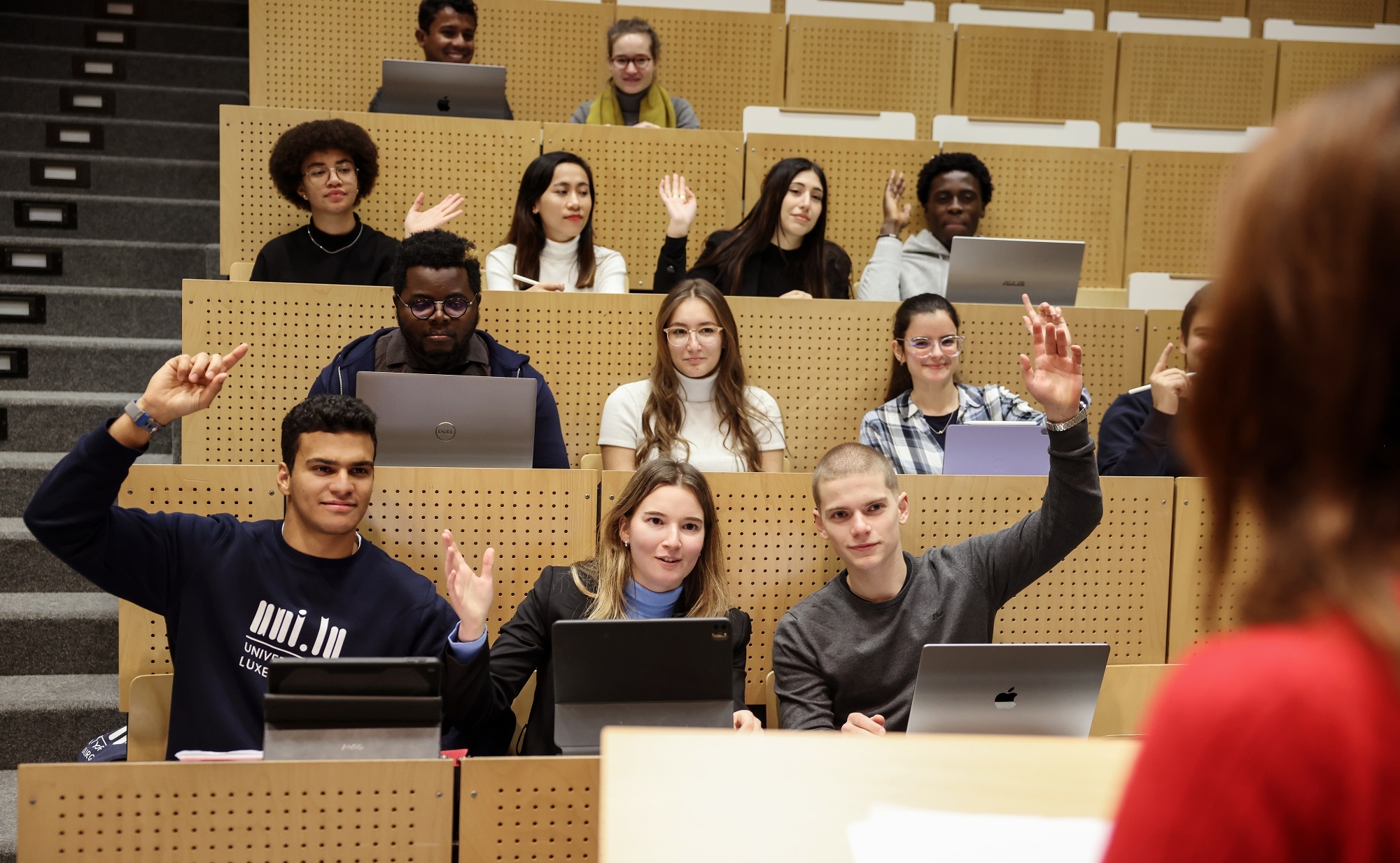 
Students raising hands in a classroom/auditorium style.