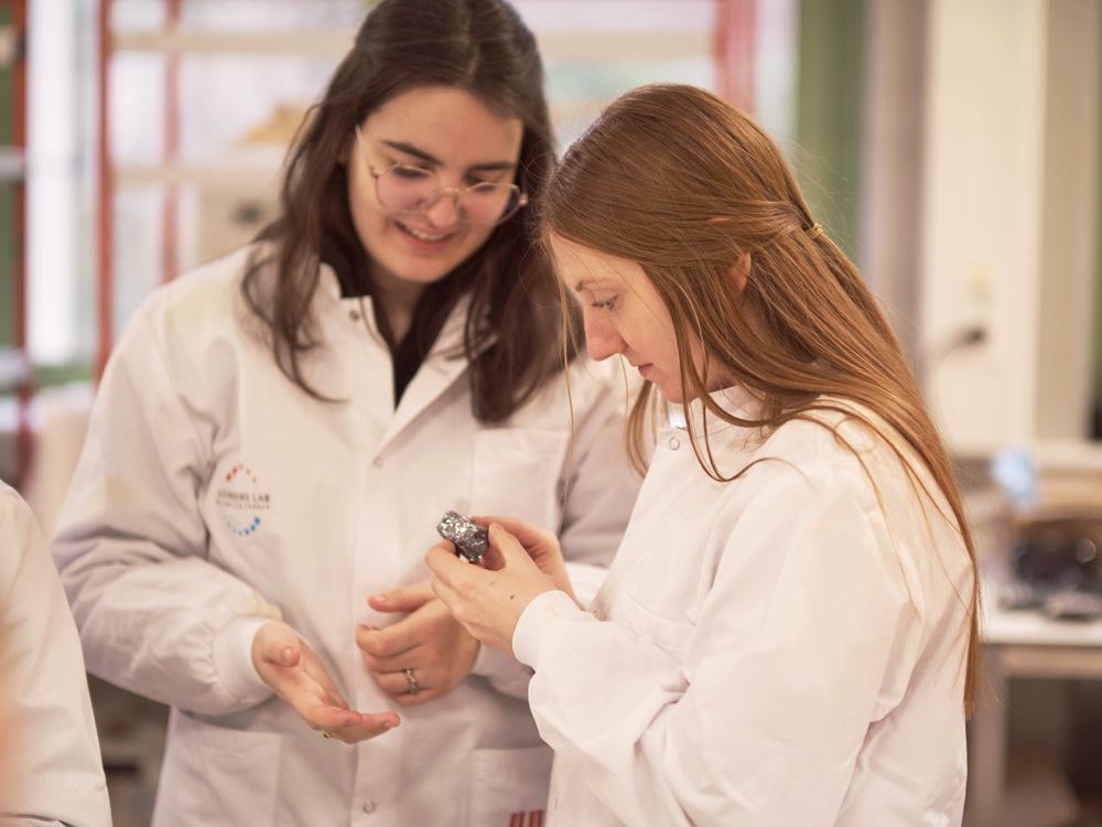 Two girls in lab coats analysing a stone.